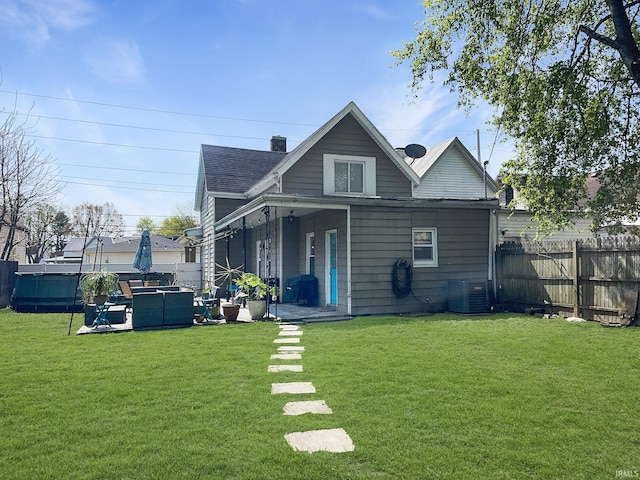 rear view of house with cooling unit, roof with shingles, a yard, and fence