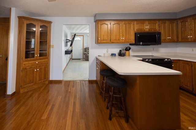 kitchen with a kitchen bar, brown cabinets, light countertops, and black appliances