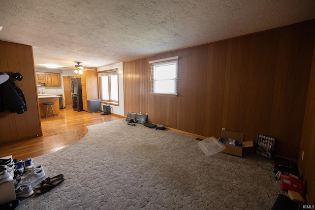 interior space with light wood-style flooring, a textured ceiling, wooden walls, and a ceiling fan