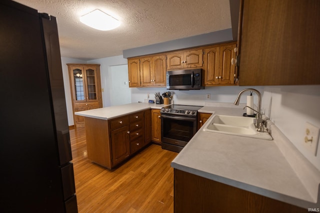 kitchen with light wood-style flooring, light countertops, a textured ceiling, stainless steel appliances, and a sink