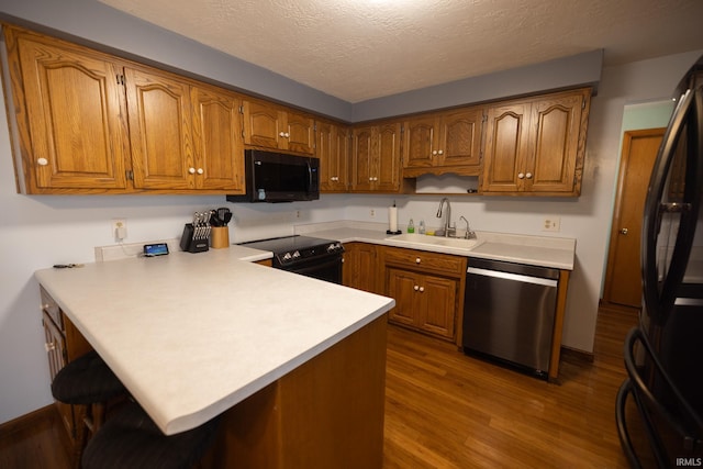 kitchen featuring brown cabinetry, a peninsula, a sink, and black appliances