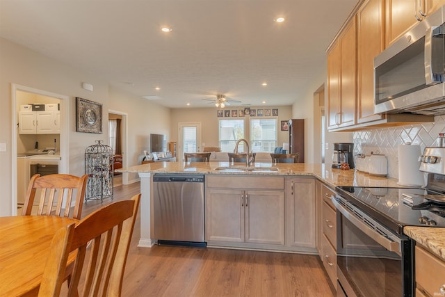 kitchen with light wood-style floors, a peninsula, light stone counters, a sink, and stainless steel appliances