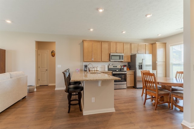kitchen featuring a sink, appliances with stainless steel finishes, a kitchen breakfast bar, a peninsula, and light brown cabinetry