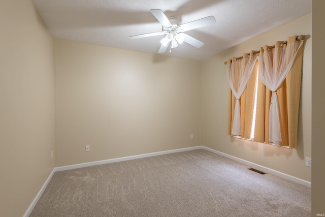 carpeted spare room with visible vents, baseboards, and a ceiling fan