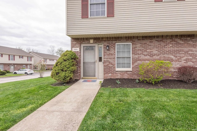 doorway to property featuring a yard, brick siding, and a residential view