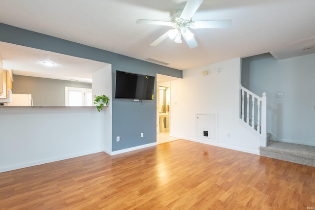 unfurnished living room with light wood-style flooring, ceiling fan, baseboards, and stairs