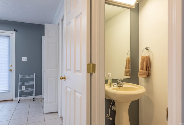 bathroom featuring a textured ceiling, a sink, baseboards, and tile patterned flooring