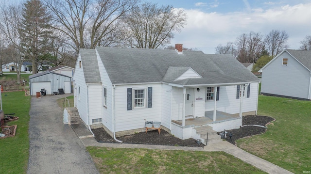 cape cod house with a chimney, a detached garage, a front lawn, an outbuilding, and a shingled roof