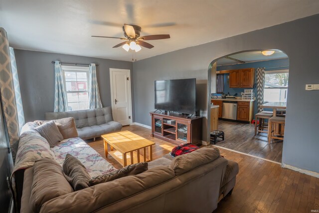 living room with arched walkways, dark wood-style floors, baseboards, and a ceiling fan