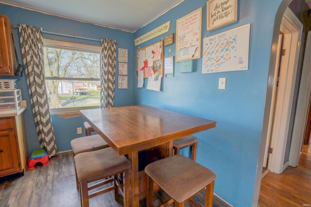 dining space featuring arched walkways, baseboards, and wood finished floors