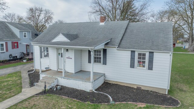 view of front of home with a front yard, roof with shingles, covered porch, and a chimney