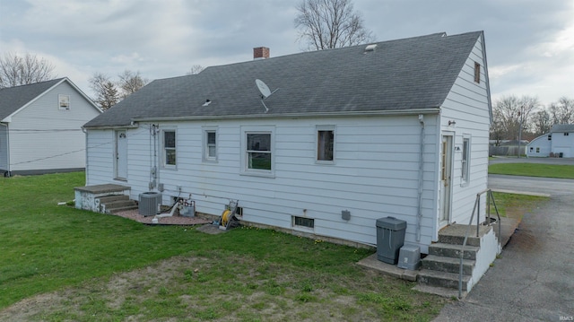back of property with roof with shingles, a chimney, and a lawn