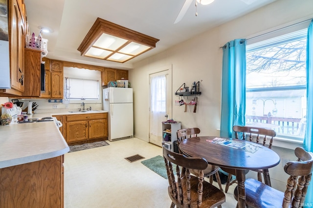 kitchen featuring brown cabinets, light countertops, visible vents, a sink, and white appliances
