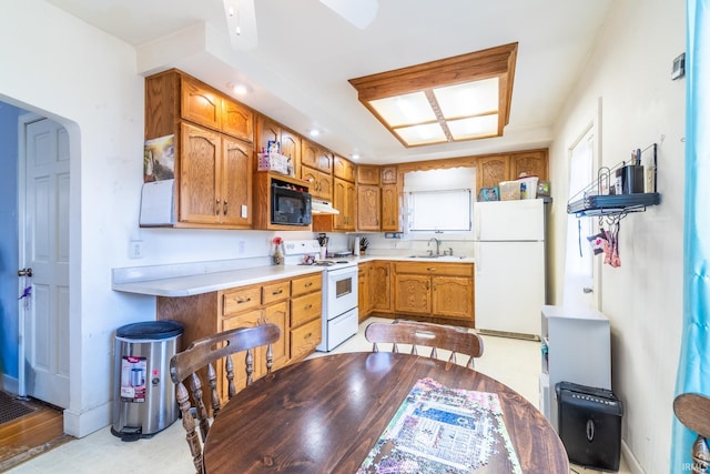 kitchen with a sink, white appliances, brown cabinets, light countertops, and under cabinet range hood