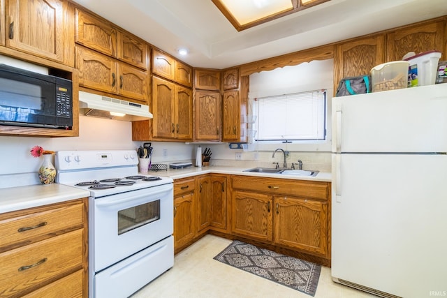 kitchen featuring brown cabinets, under cabinet range hood, light countertops, a sink, and white appliances