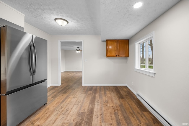 kitchen with ceiling fan, freestanding refrigerator, a textured ceiling, brown cabinets, and baseboard heating