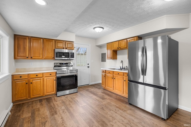 kitchen featuring a textured ceiling, light countertops, appliances with stainless steel finishes, a sink, and wood finished floors
