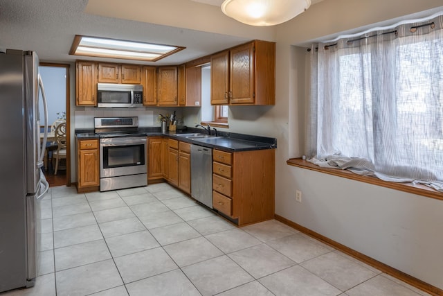 kitchen featuring brown cabinetry, appliances with stainless steel finishes, a sink, and dark countertops