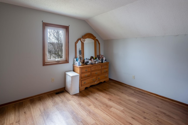 bedroom featuring visible vents, baseboards, light wood-type flooring, a textured ceiling, and lofted ceiling