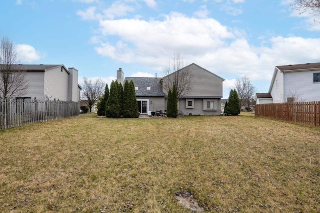 back of house with a yard, fence, and a chimney