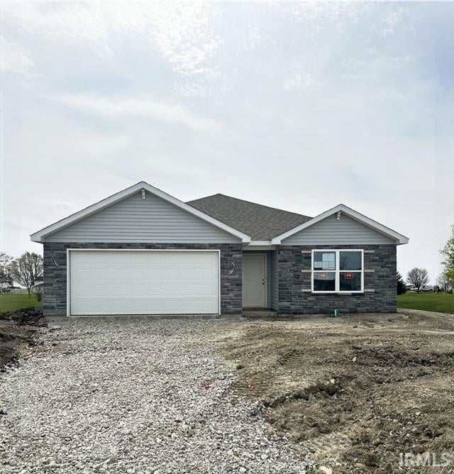 single story home featuring an attached garage, stone siding, and gravel driveway