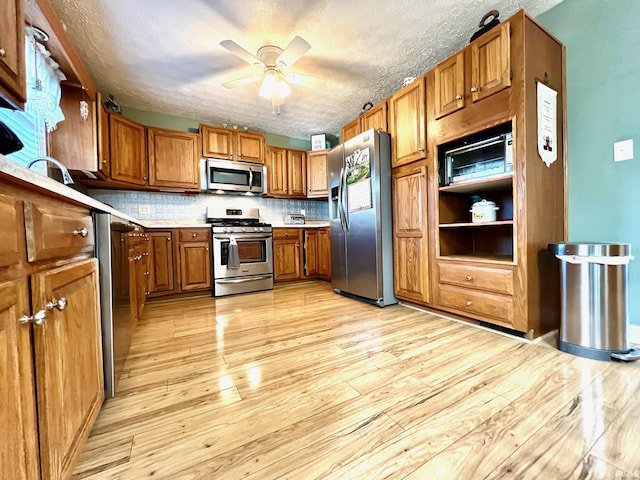 2119 Windwood Dr, Bedford, IN 47421 - kitchen featuring light wood-type flooring, light countertops, brown cabinets, ceiling fan, and stainless steel appliances