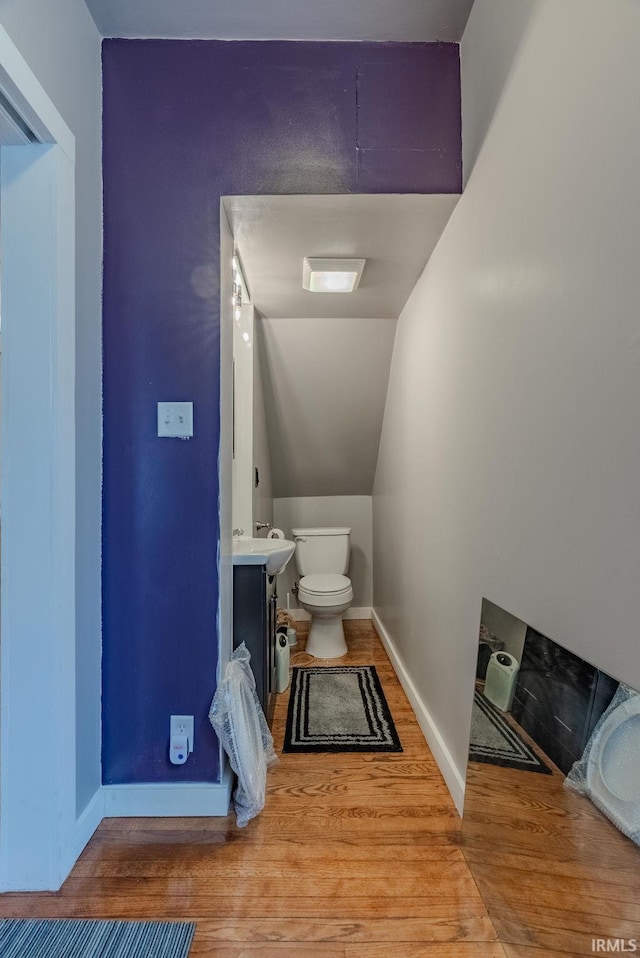 bathroom featuring vanity, toilet, wood finished floors, lofted ceiling, and baseboards