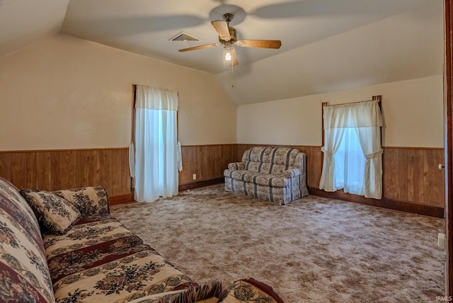 carpeted living room with visible vents, wood walls, vaulted ceiling, and a wainscoted wall