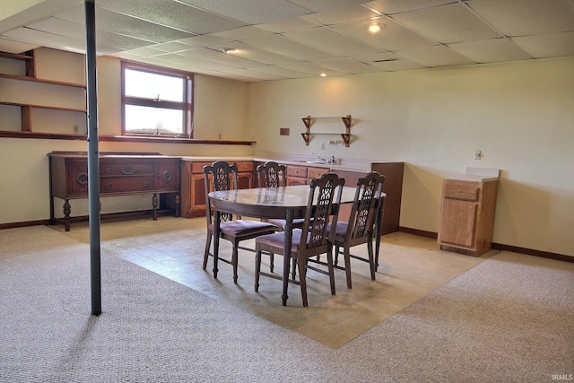 dining space featuring light floors, baseboards, a drop ceiling, and indoor bar