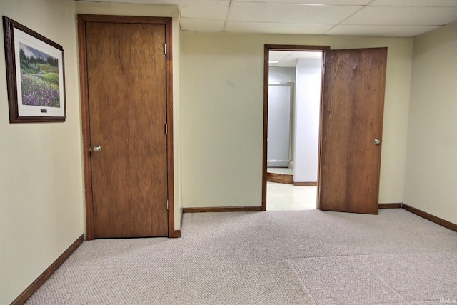 unfurnished bedroom with light carpet, baseboards, and a drop ceiling