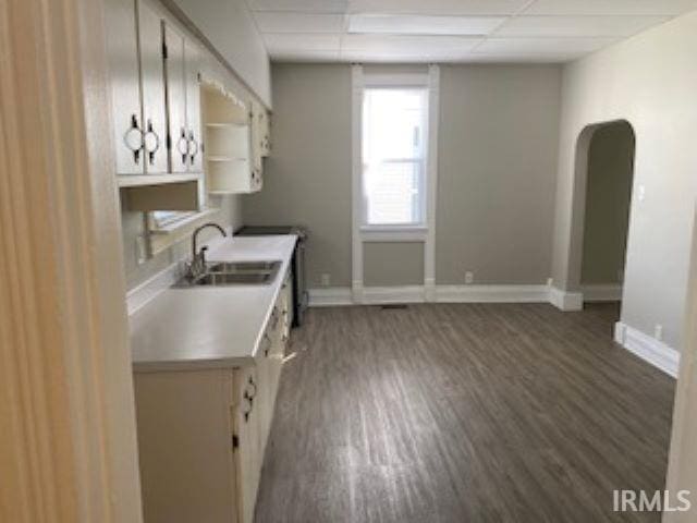 kitchen featuring dark wood-type flooring, a drop ceiling, a sink, light countertops, and baseboards