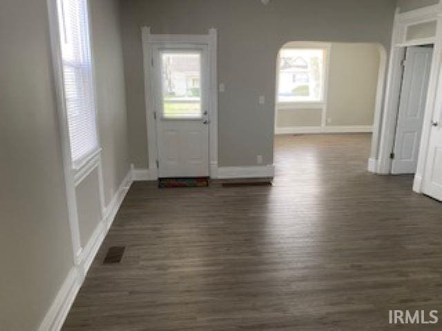 entrance foyer featuring visible vents, baseboards, arched walkways, and dark wood-style floors