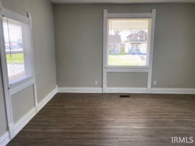 empty room featuring visible vents, baseboards, and dark wood-style floors