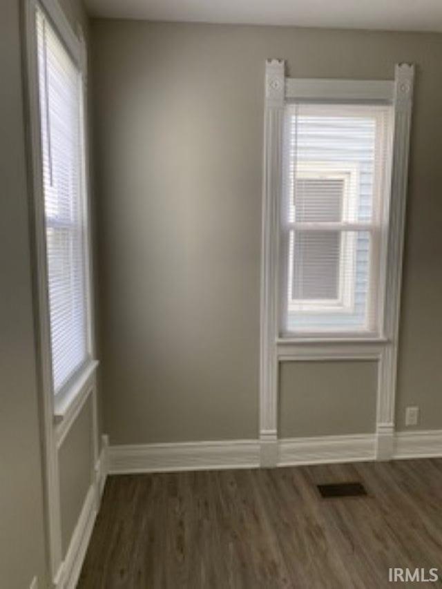 unfurnished room featuring dark wood-type flooring, visible vents, baseboards, and a healthy amount of sunlight
