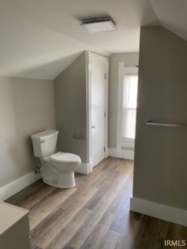 bathroom with toilet, wood finished floors, baseboards, and lofted ceiling