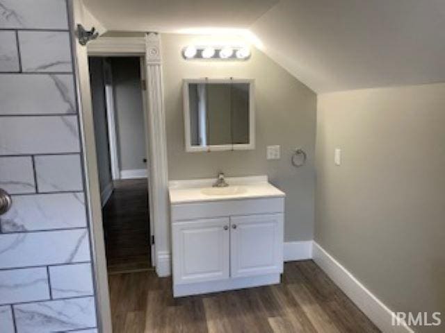 bathroom featuring baseboards, vanity, wood finished floors, and lofted ceiling