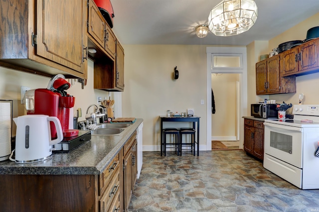 kitchen featuring an inviting chandelier, a sink, dark countertops, white appliances, and stone finish flooring