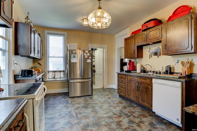 kitchen with white appliances, stone finish flooring, a chandelier, dark countertops, and baseboards