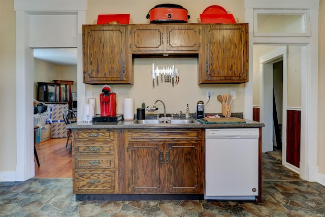 kitchen with stone finish floor, a sink, white dishwasher, and dark countertops