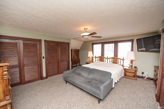 bedroom featuring baseboards, ceiling fan, a textured ceiling, multiple closets, and light carpet
