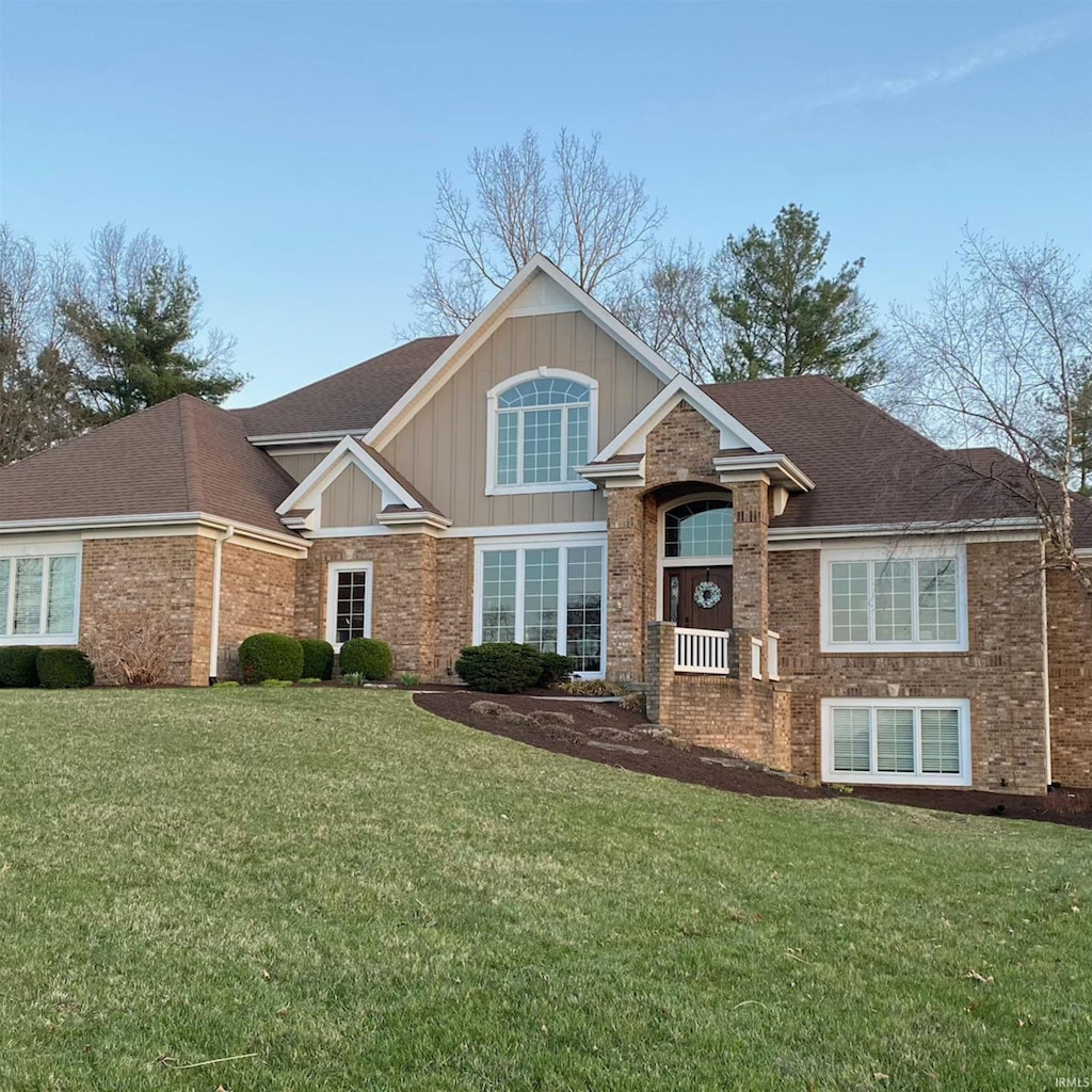 view of front facade with board and batten siding, a front lawn, brick siding, and roof with shingles
