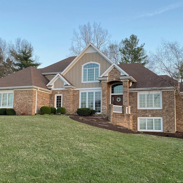 view of front facade with board and batten siding, a front lawn, brick siding, and roof with shingles