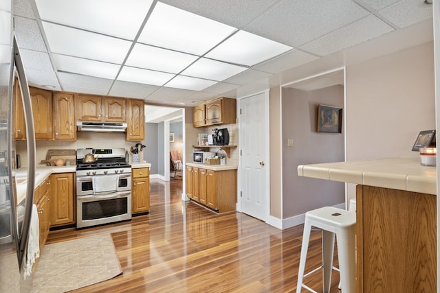 kitchen with stainless steel appliances, light wood-style flooring, baseboards, a paneled ceiling, and ventilation hood