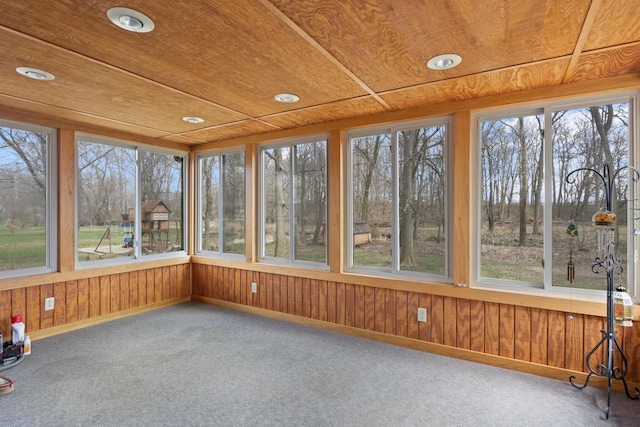 unfurnished sunroom with wood walls, baseboards, wooden ceiling, and carpet flooring