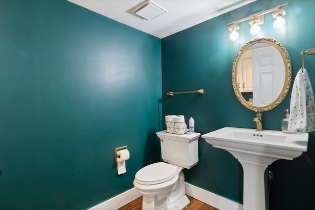 half bathroom featuring a sink, wood finished floors, baseboards, toilet, and visible vents