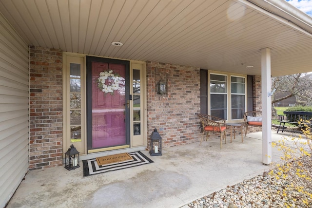 view of exterior entry featuring brick siding and covered porch