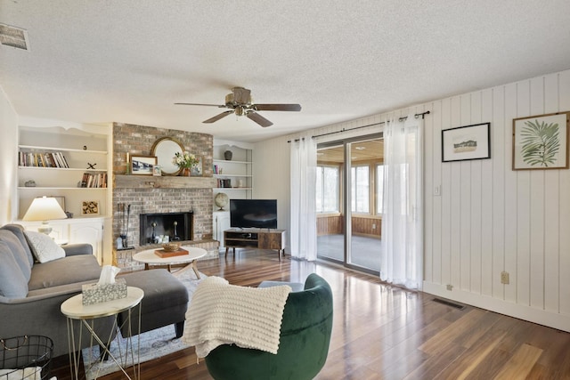 living area with a textured ceiling, visible vents, a brick fireplace, wood finished floors, and ceiling fan
