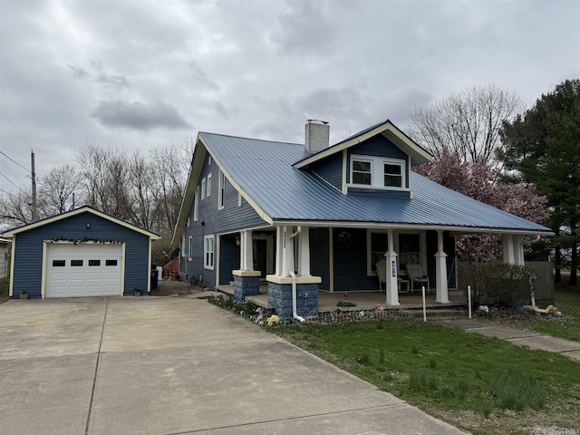 view of front facade featuring an outbuilding, a detached garage, a chimney, metal roof, and covered porch