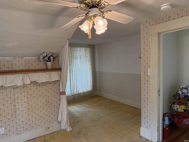 unfurnished bedroom featuring a ceiling fan, wood finished floors, wallpapered walls, a textured ceiling, and baseboards