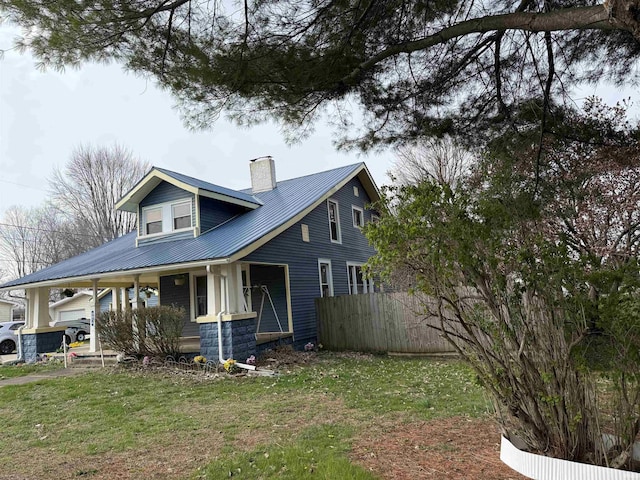 view of side of home with a chimney, metal roof, covered porch, fence, and a lawn